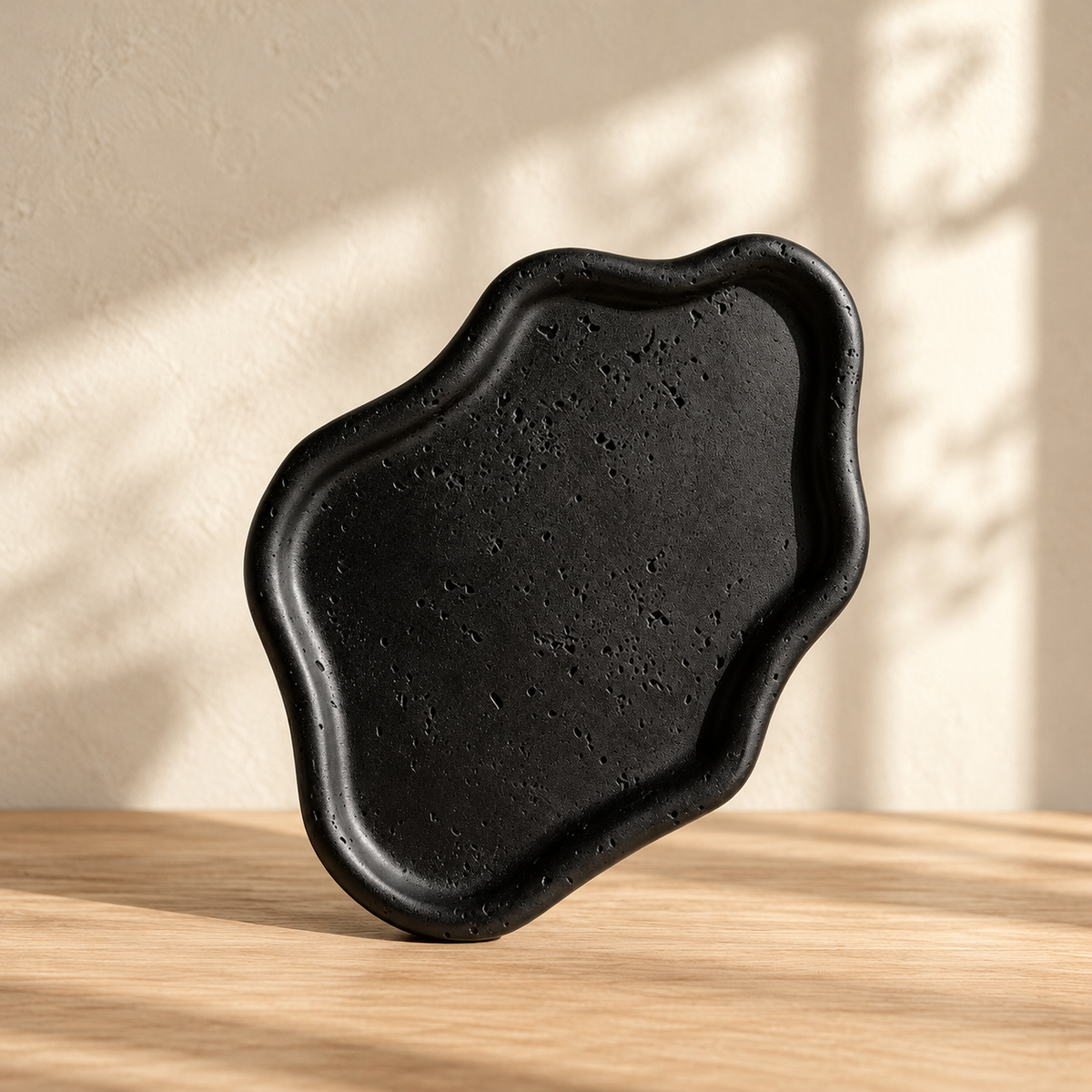 Black irregular display tray with a low wavy rim on warm oak against a cream wall.
